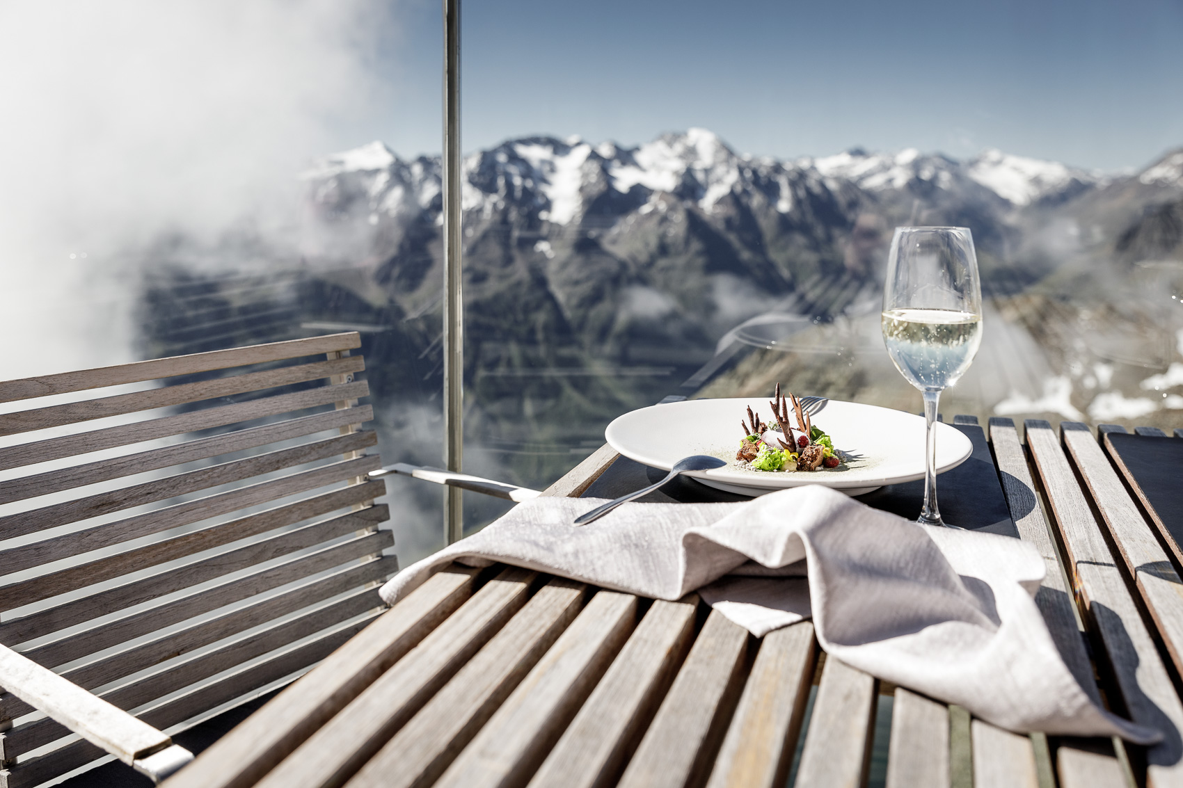 Gourmet-Essen und Weißwein auf der Terrasse des Ice-Q Restaurants am Gaislachkogel in Sölden, mit Panoramablick auf die schneebedeckten Berge. Das Sternerestaurant auf 3.000m bietet alpine Genusserlebnisse.
