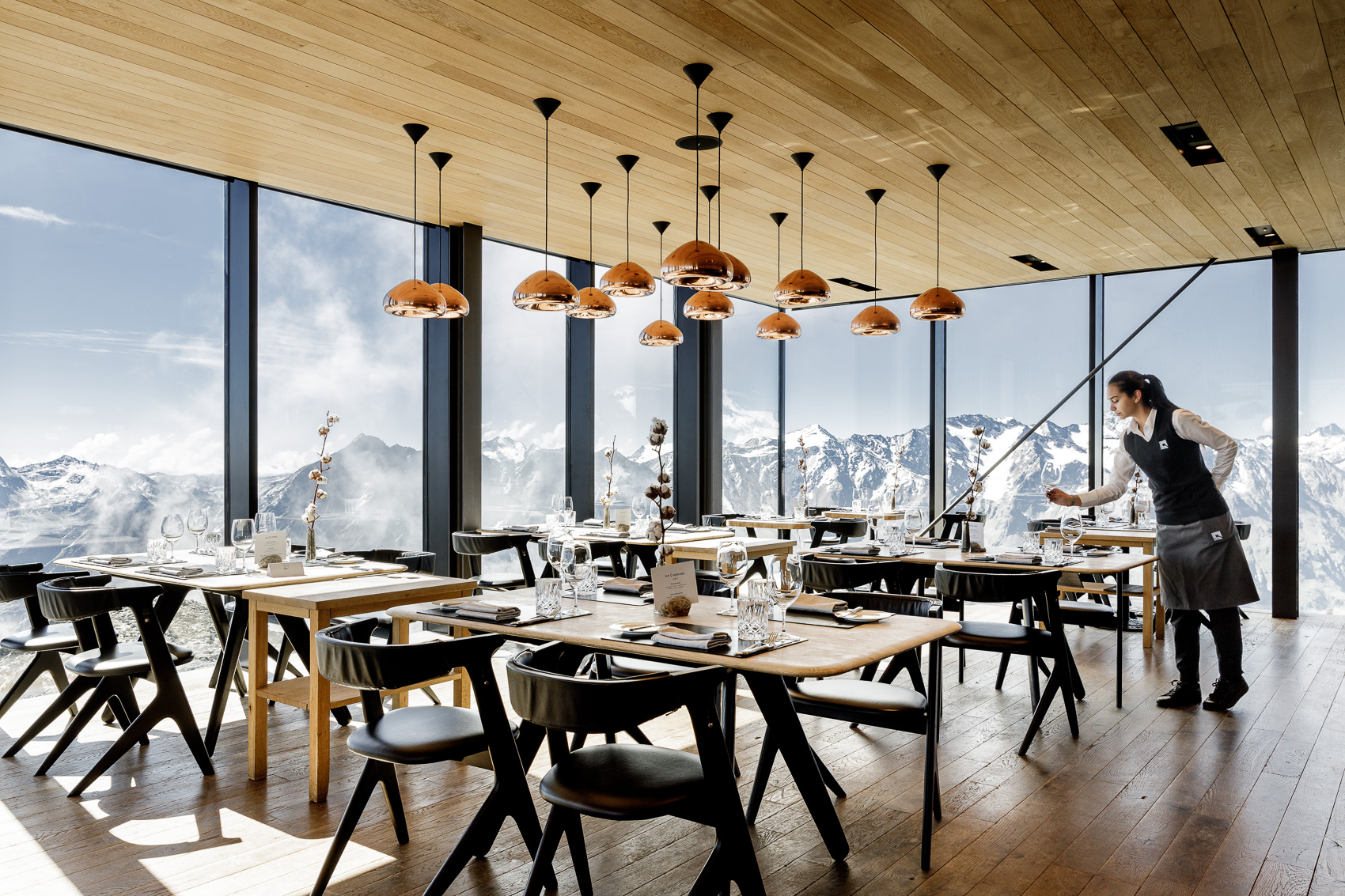 Das Ice-Q Gourmetrestaurant auf dem Gaislachkogel in Sölden bietet Sterne-Küche in modernem Ambiente mit Panoramafenstern und beeindruckendem Alpenblick. Eine Servicekraft bereitet die stilvoll eingedeckten Tische vor.