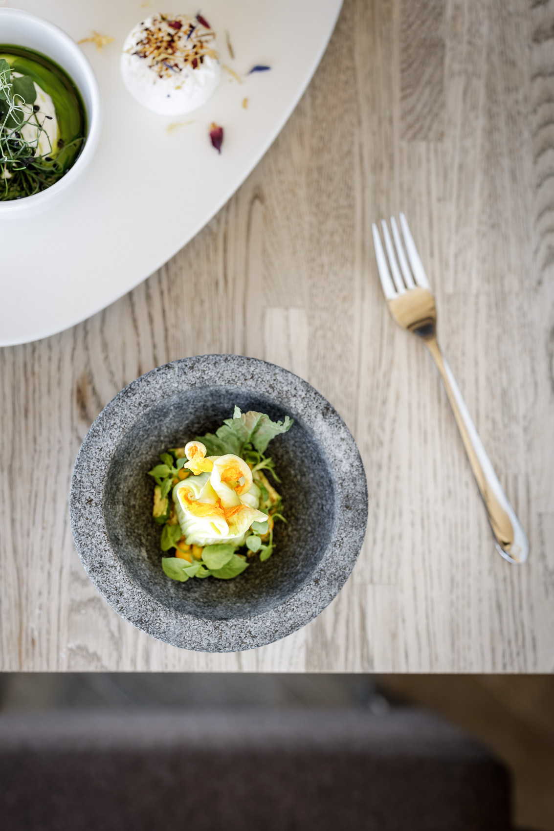 Fein angerichtete Gerichte, darunter eine Kreation in einer Steinschale und ein grüner Dip, stehen auf einem Holztisch im Gourmet Restaurant Ice-Q am Gaislachkogel. Die Sterne Küche auf 3000m Höhe in Sölden verspricht einzigartige kulinarische Erlebnisse.