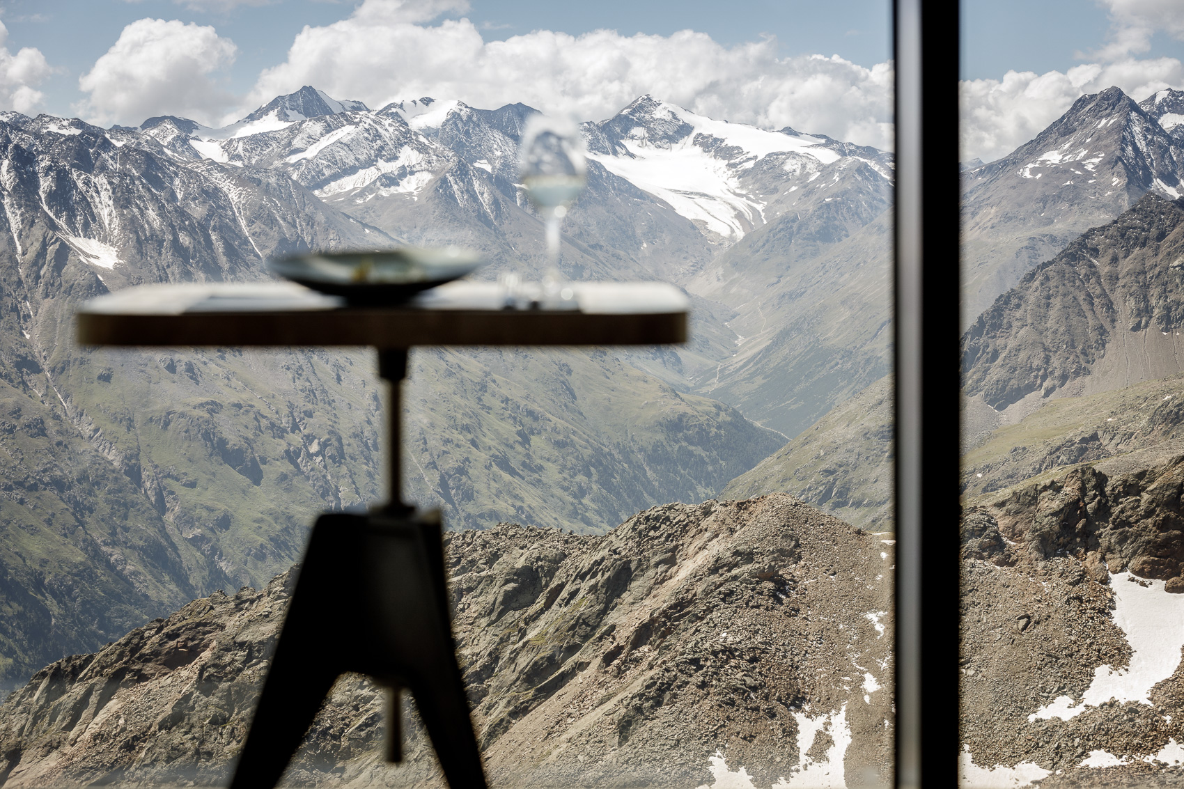 Tisch mit Speis und Weinglas im Ice Q, Sölden, vor der atemberaubenden Kulisse der verschneiten Ötztaler Alpen. Dieser Blick auf 3000m Höhe unterstreicht das einzigartige Gourmet-Erlebnis der Sterne-Küche.