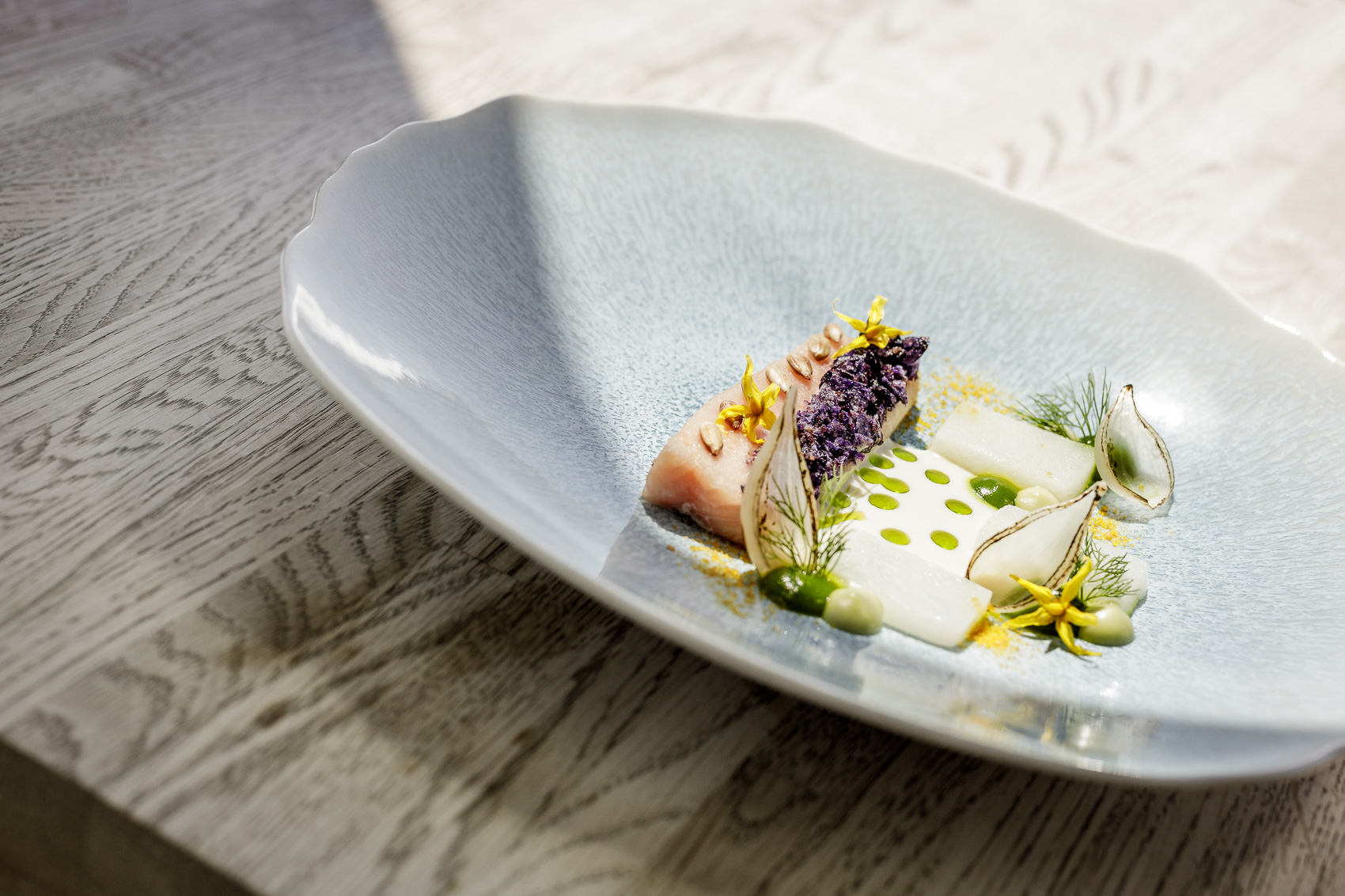 Ein kunstvoll angerichtetes Gourmetgericht, präsentiert im Ice-Q Restaurant auf dem Gaislachkogel in Sölden. Dieses Beispiel der Sterne-Küche auf 3000m Höhe zeigt helle Fisch- oder Fleischstücke mit Lavendel, hellem Gemüse und grünen Saucenspritzern.