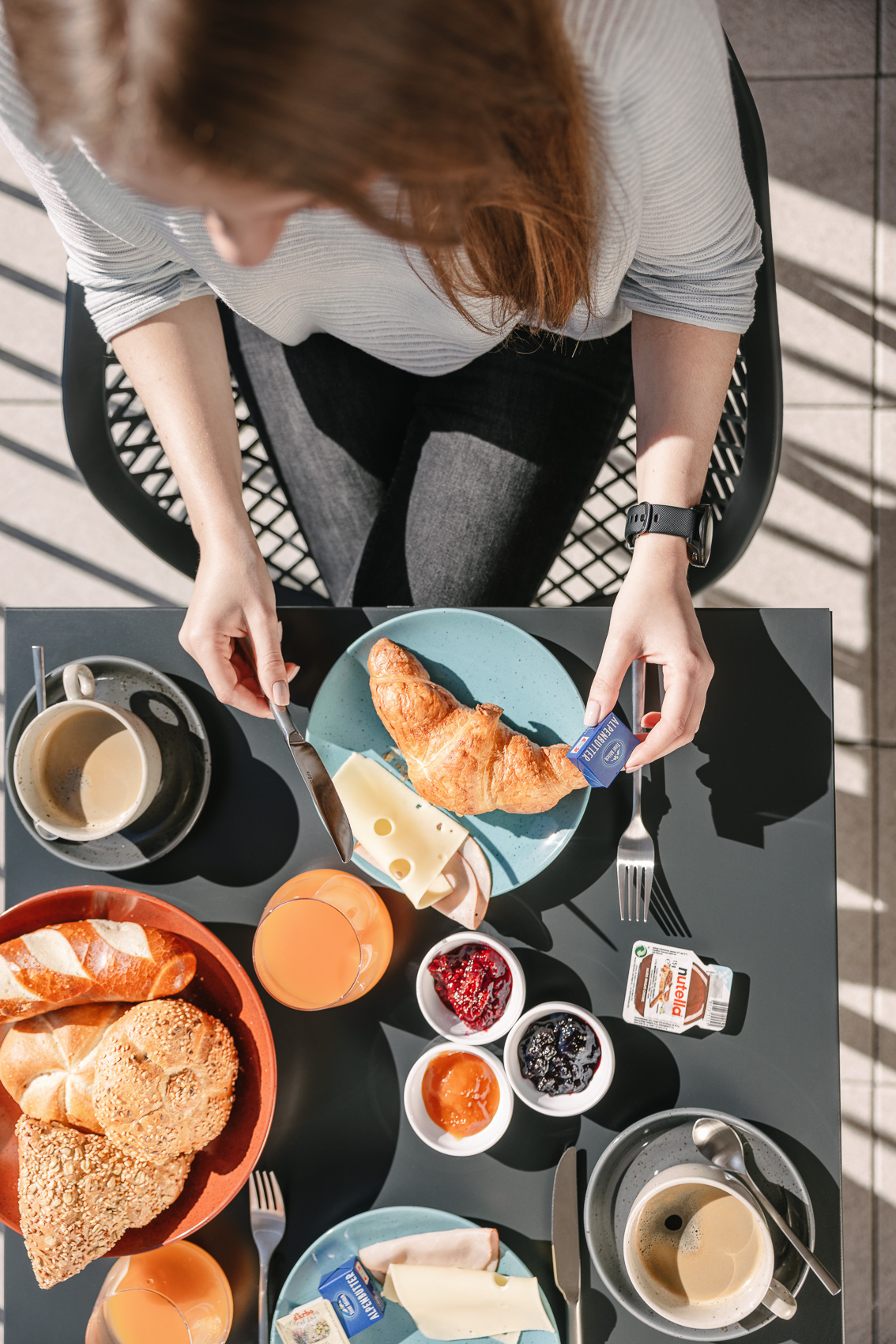 Ein Gast genießt ein reichhaltiges Frühstück mit Croissant, Aufschnitt und Marmeladen auf einer sonnigen Terrasse in Oetz, perfekt für MyAlps Tirol. Das Bild zeigt einen entspannten Start in den Tag, wie er in Hotels dieser Region üblich ist.