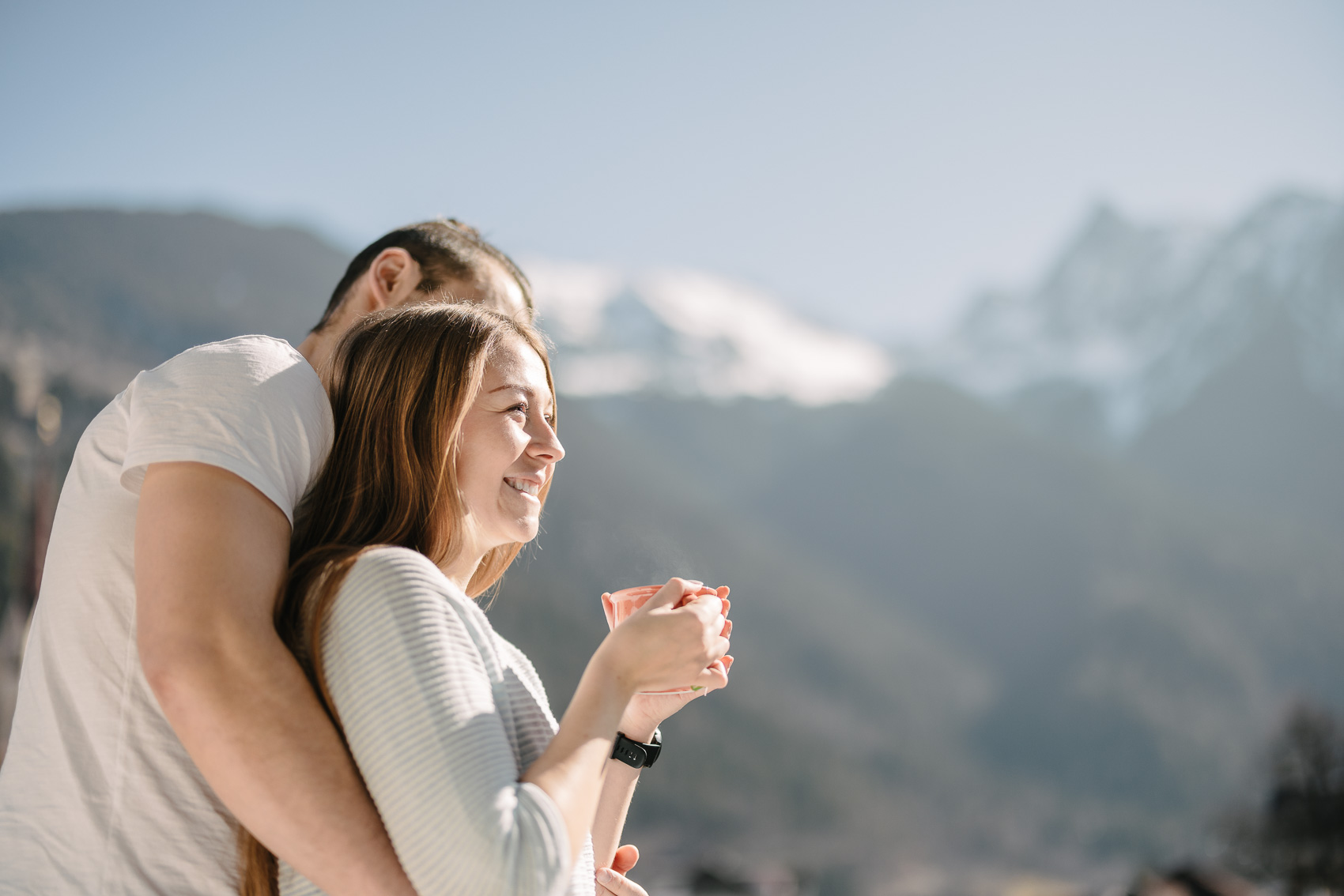 Ein lächelndes Paar genießt den Morgen auf einem Balkon im MyAlps Tirol in Oetz, mit verschneiten Berggipfeln im Hintergrund – eine Szene der Hotelfotografie, die Entspannung einfängt.