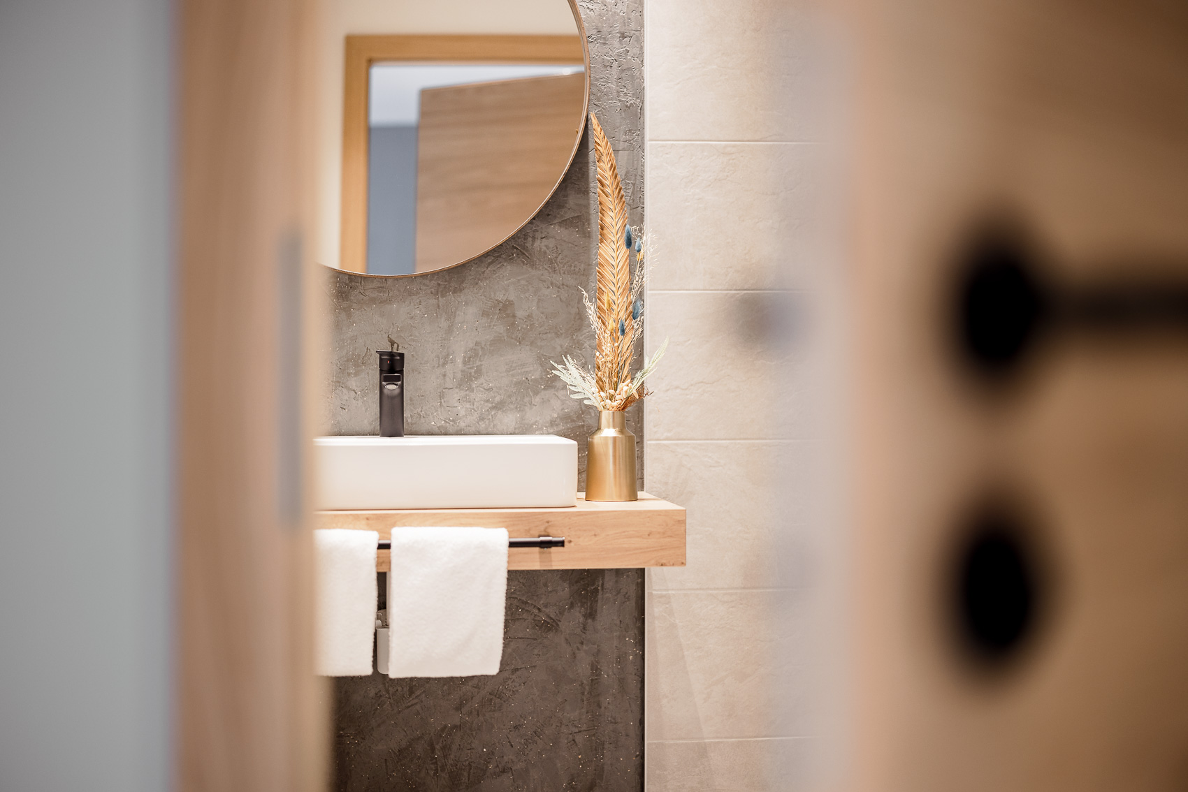 Modernes Badezimmer mit Waschtisch, rundem Spiegel und Dekoration. Ein Detail der Hotelfotografie von MyAlps Tirol in Oetz, das Eleganz und alpinen Stil verbindet.