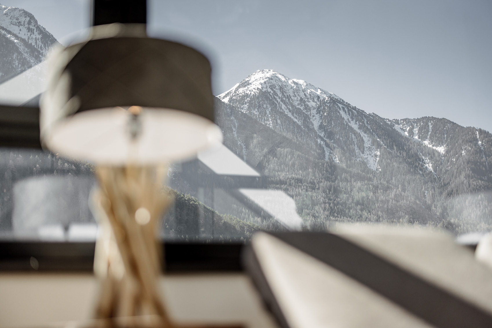 Ein verschneiter Berggipfel in den Tiroler Alpen, gesehen durch ein hotellartiges Fenster, das teilweise von einer stilvollen Lampe verdeckt wird. Es vermittelt die beeindruckende Aussicht, die Gäste von MyAlps Tirol in Oetz genießen können.